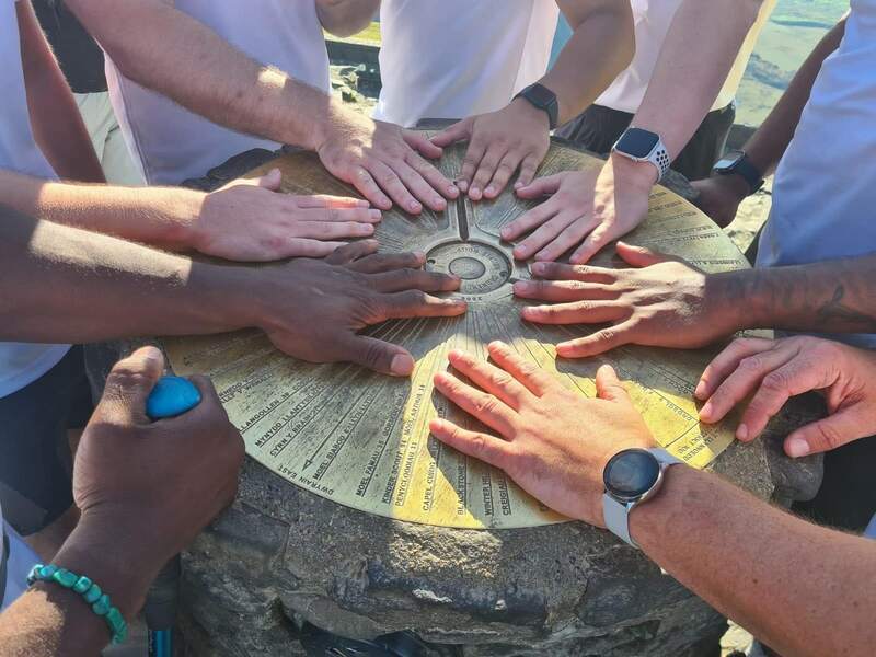 Hands placed together on the summit marker at the top of the mountain