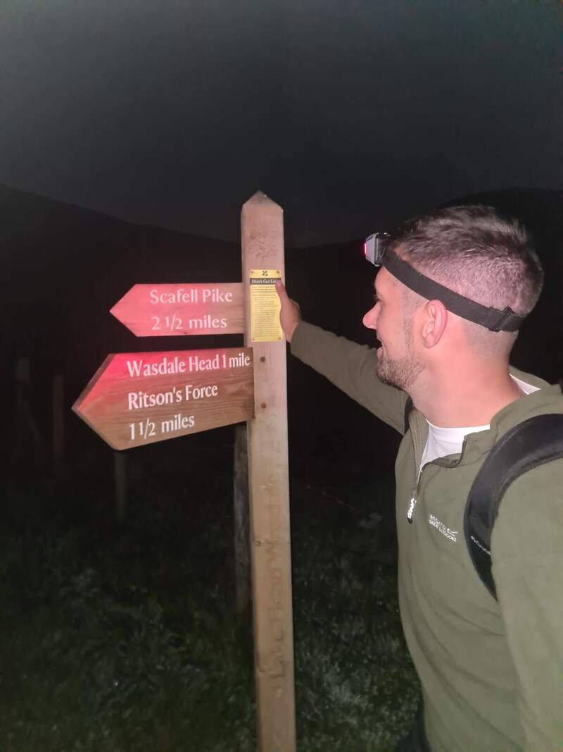 A walker with a head torch reading the Scafell Pike signpost at night
