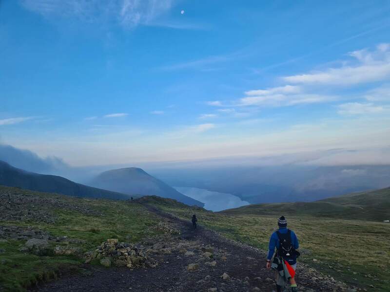 A walker heading down the mountain with a lake in the valley below